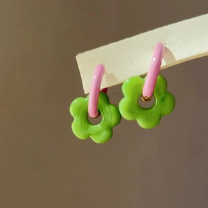 Detail of pink and green floral drop earrings on a white display card with soft lighting