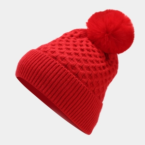 Detail of red waffle-knit winter beanie featuring a matching faux fur pom-pom and ribbed cuff