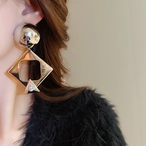 Close-up of golden geometric earrings with crystals worn by model on a beige background