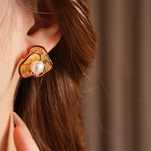 Macro detail of gold braided texture earrings with white pearl worn by a model