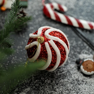 Rote Weihnachtskugel mit weißen Plüschspiralen vor festlichem Hintergrunddekor