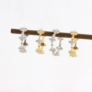 Macro shot of silver and gold clover earrings with sparkling diamonds on a wooden stand