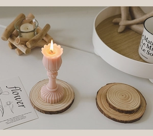 Macro view of a lit flower-shaped pink candle on a rustic wooden slice base