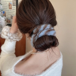 Dettaglio di elastici in peluche a righe indossati su uno chignon e al polso per un look elegante