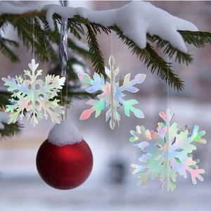 Iridescent snowflake pendants and red bauble on snow-covered Christmas tree branches