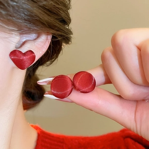 Dettaglio degli orecchini rossi a cuore e tondi con texture in seta su una modella