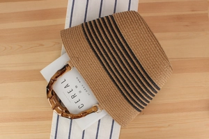 Detail of woven straw handbag with black stripes, bamboo handle and gold metal rings