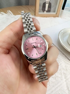 Close-up of a silver watch with a pink dial and calendar display in a cozy setting