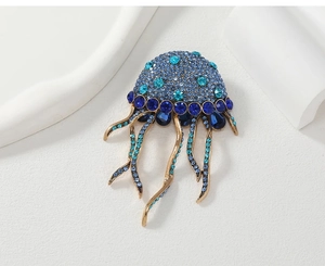 Close-up of jellyfish brooch with blue crystals and tassels on a white artistic base