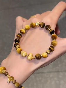 Nahaufnahme eines Tigerauge-Armbands mit Goldherz-Anhänger am Handgelenk einer Frau