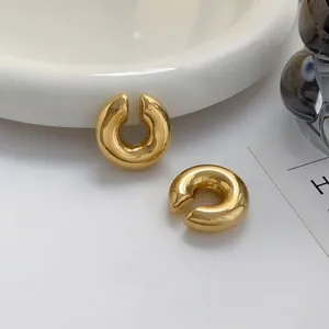 Polished chunky gold C-shaped clip-on hoop earrings on minimalist white tray