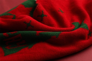 Close-up of red and green knitted Christmas scarf featuring reindeer and snowflake patterns