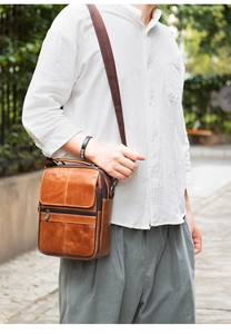 Brown leather men's messenger bag with adjustable strap shown in an outdoor lifestyle setting