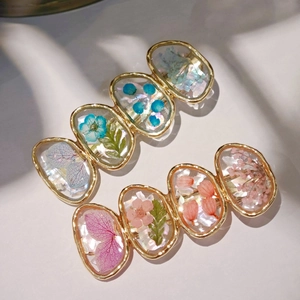 Pair of gold shell resin hair clips with real dried flowers on white fabric