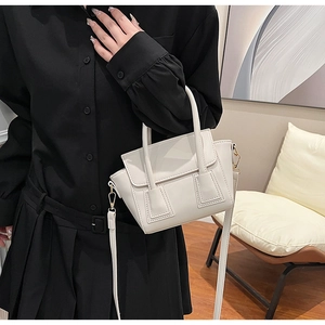 Detail of white PU bucket bag featuring a trapezoidal design and elegant gold hardware