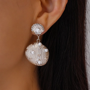 Detail view of silver shell-shaped earrings with pearls on female model's ear