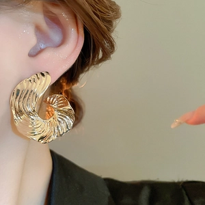 Close-up of a large golden geometric earring with unique wavy texture on a female model