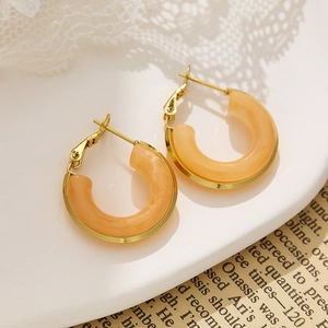 Macro shot of gold square hoop earrings with orange resin on white lace tray