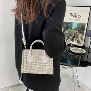 Chic beige tweed handbag with gold threads and white handle shown in a cafe setting