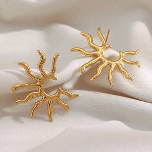 Detailed close-up of 18K gold plated stainless steel sunburst stud earrings on white fabric