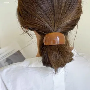 Close-up of a brown acetate curved ponytail clip worn on a woman's hair in a minimalist style