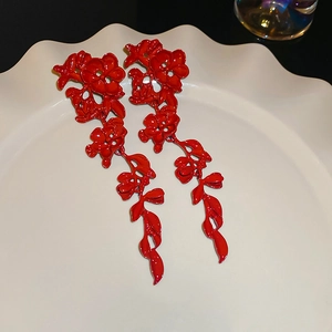 Detailed close-up of long red floral drop earrings on a white decorative plate