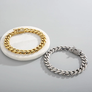 Close-up of gold and silver Cuban link bracelets with diamond-encrusted clasps on marble