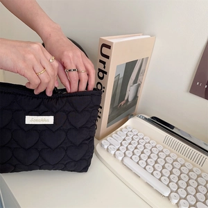 Detail of black quilted heart makeup bag being opened on a desk with a vintage keyboard