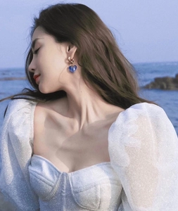 Blue heart-shaped glass earrings worn by a model in a beach setting with sun light