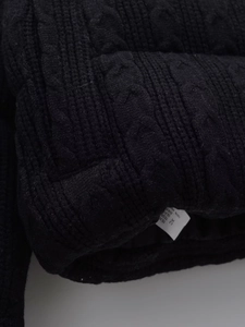 Close-up detail of black knitted fabric with chunky cable weave pattern on the jacket