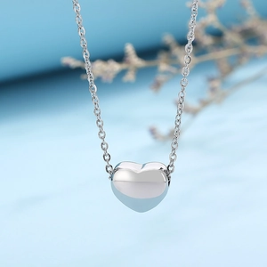 Close-up of polished silver heart pendant on a thin chain over a soft blue background