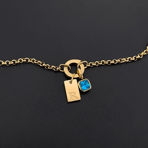 Collar de acero de titanio dorado con placa grabada con la letra R y cristal azul.