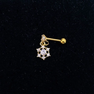 Close-up of golden snowflake stud earring with clear zircon inlay on textured surface