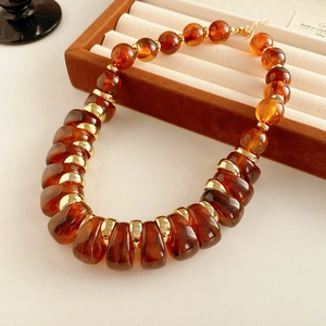 Détail du collier de perles ambrées et dorées posé sur un plateau à bijoux en velours