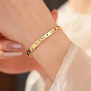Bracelet jonc plaqué or avec zircons et gravures d'étoiles sur poignet féminin