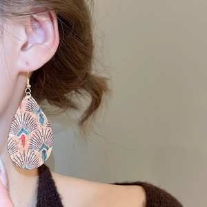 Detail shot of vintage leather teardrop earrings with feather patterns on a model