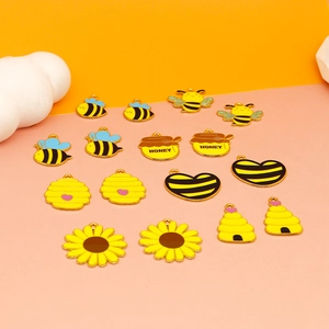 Flat lay of 14 bee-themed enamel honey charms, including sunflowers and hives on pink surface