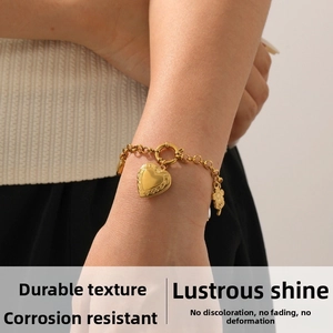 Detail of a gold heart pendant bracelet with a sunflower charm worn on a wrist