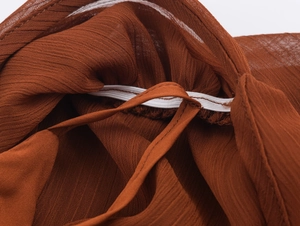 Detailansicht der braunen Faltenstoffstruktur mit weißen elastischen Nahtdetails