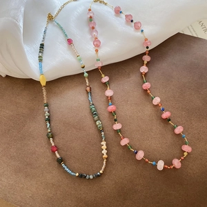 Detail of colorful beads and pink crystal necklaces on white silk with leather background