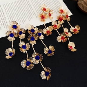 Close-up of gold hollow flower tassel earrings with vibrant red and blue gemstone centers