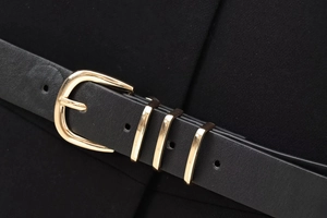 Détail d'une ceinture en cuir noir avec boucle dorée et trois passants métalliques