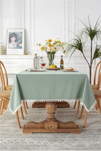 Detail of green cotton tablecloth with white decorative tassels on a wooden dining table