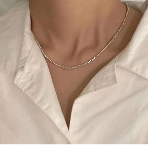 Gros plan sur un collier minimaliste en perles d'argent facettées avec chemise blanche