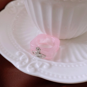 Close-up of pink resin ring with silver saturn logo on a white ceramic plate