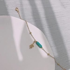 Detail of gold thin chain bracelet featuring a turquoise bead and snake charm on a display