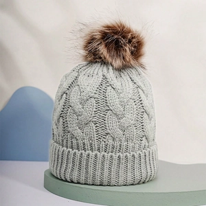 Detailed view of grey cable knit texture and soft faux fur pompom on winter hat