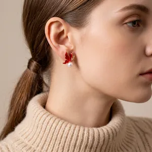 Élégantes boucles d'oreilles papillon en perles dorées avec ailes en émail rouge sur modèle