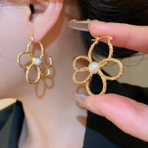 Detail of gold flower earrings with hammered texture and a white pearl center
