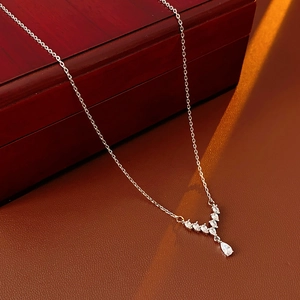 Close-up of V-shaped silver necklace with teardrop zircon pendant on a leather surface